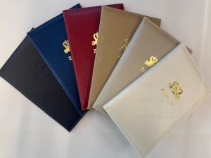 Een foto van de te kiezen trouw- of partnerschapboekjes in waaier gelegd. Van links naar rechts de kleuren blauwzwart, blauw, bordeauxrood, taupe, zand en wit. Op de voorkant van de boekjes is in goud het wapen van de gemeente Zaanstad met daaronder het woord ‘Zaanstad’ te zien. Op het blauwzwarte boekje is het logo en de naam Zaanstad niet goud, maar dezelfde kleur als het boekje.
